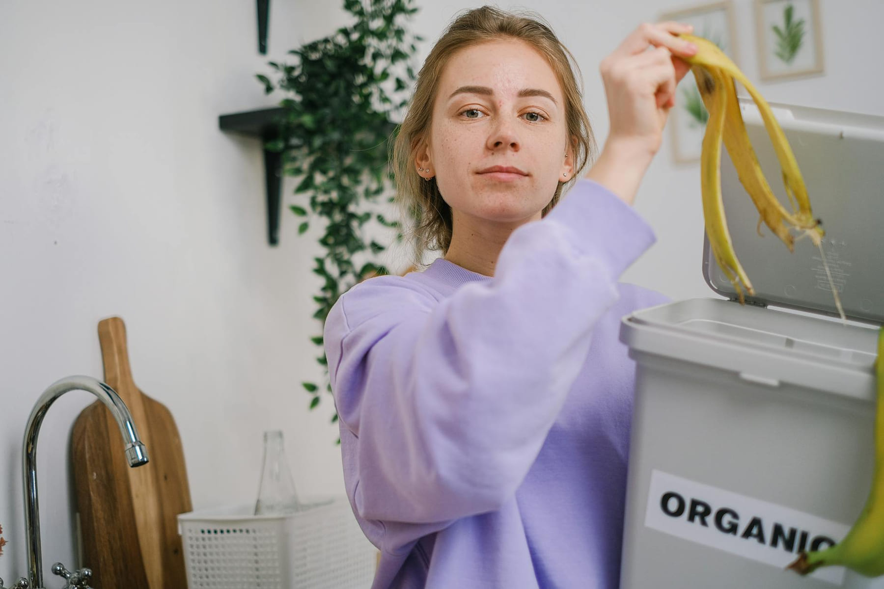 Woman disposing banana peel in organic bin at home kitchen, promoting eco-friendly lifestyle. on Earth Wise Budget