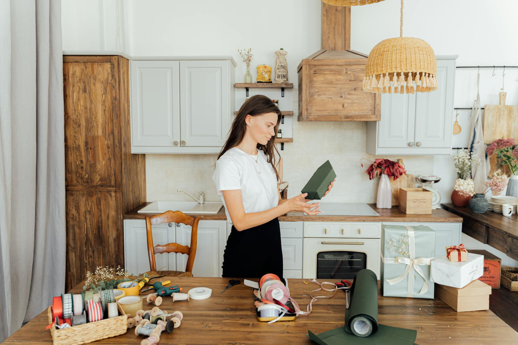 A woman wrapping presents in a cozy kitchen with ribbon and paper around. on Earth Wise Budget