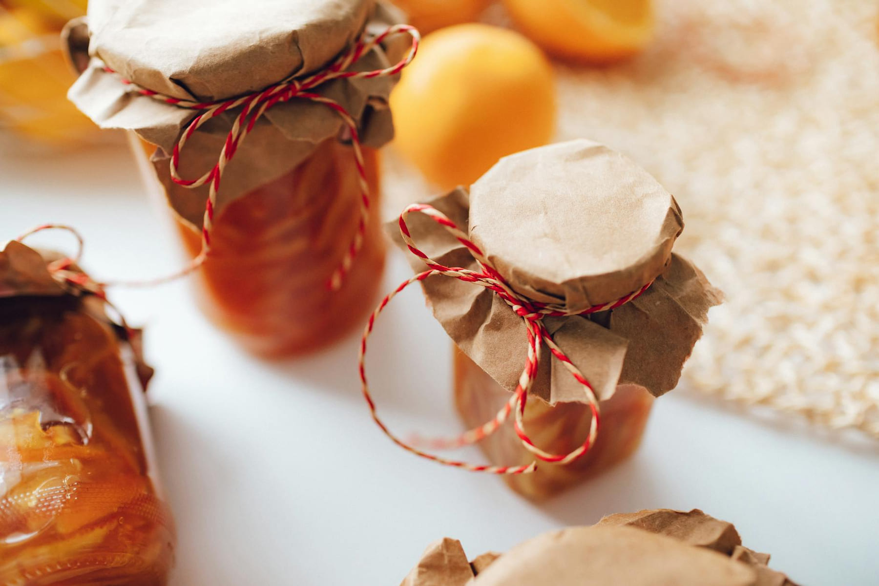 A close-up image of homemade preserves in jars wrapped with paper and string, indoors. on Earth Wise Budget