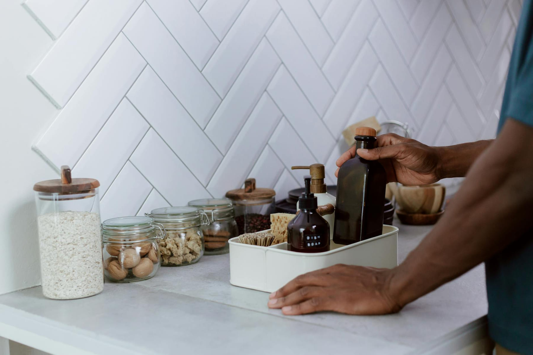 A person tidily organizes a kitchen counter with reusable glass jars and bottles. on Earth Wise Budget
