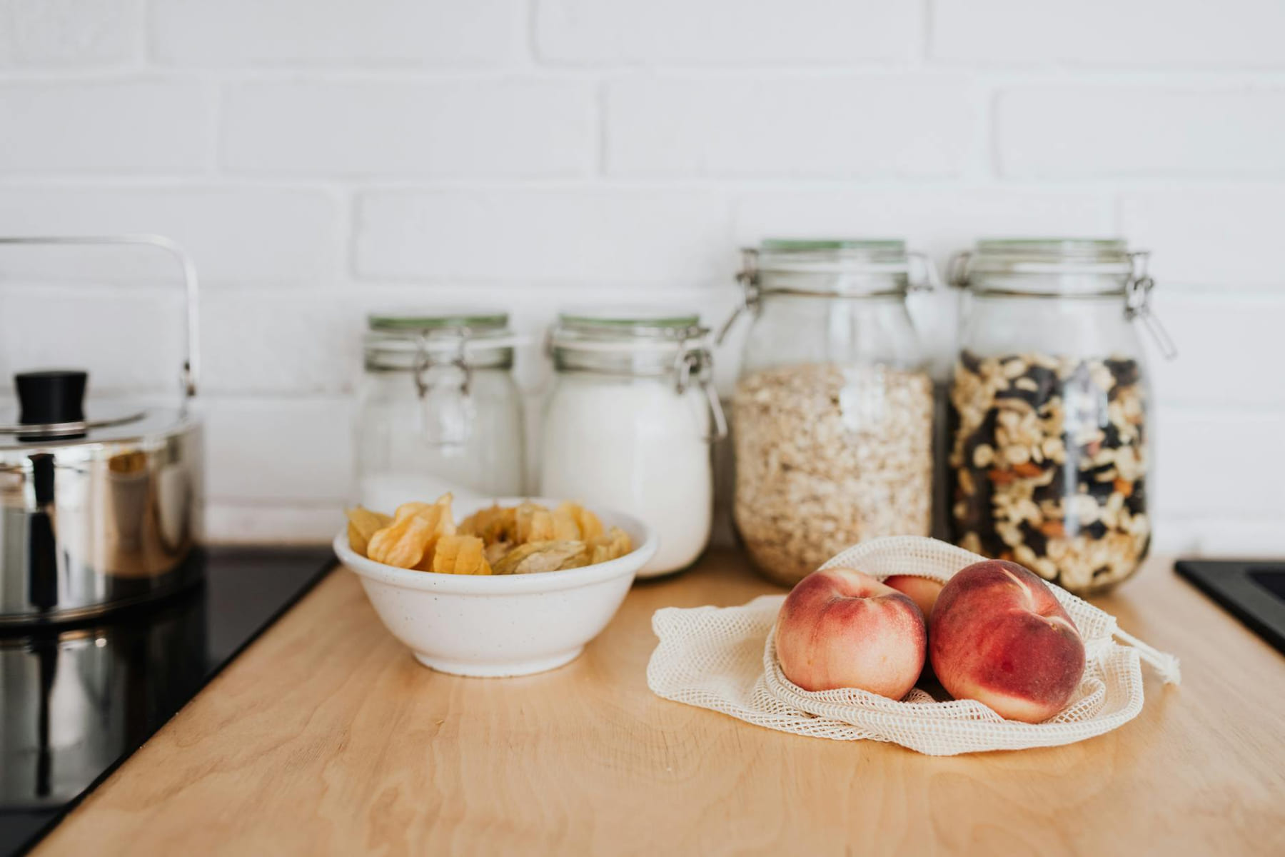 A selection of zero waste kitchen essentials with reusable jars and fresh fruit on a wooden countertop. on Earth Wise Budget