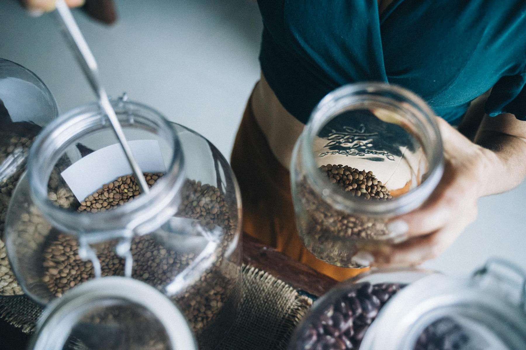 Person refilling glass jars with seeds in eco-friendly refill store. on Earth Wise Budget