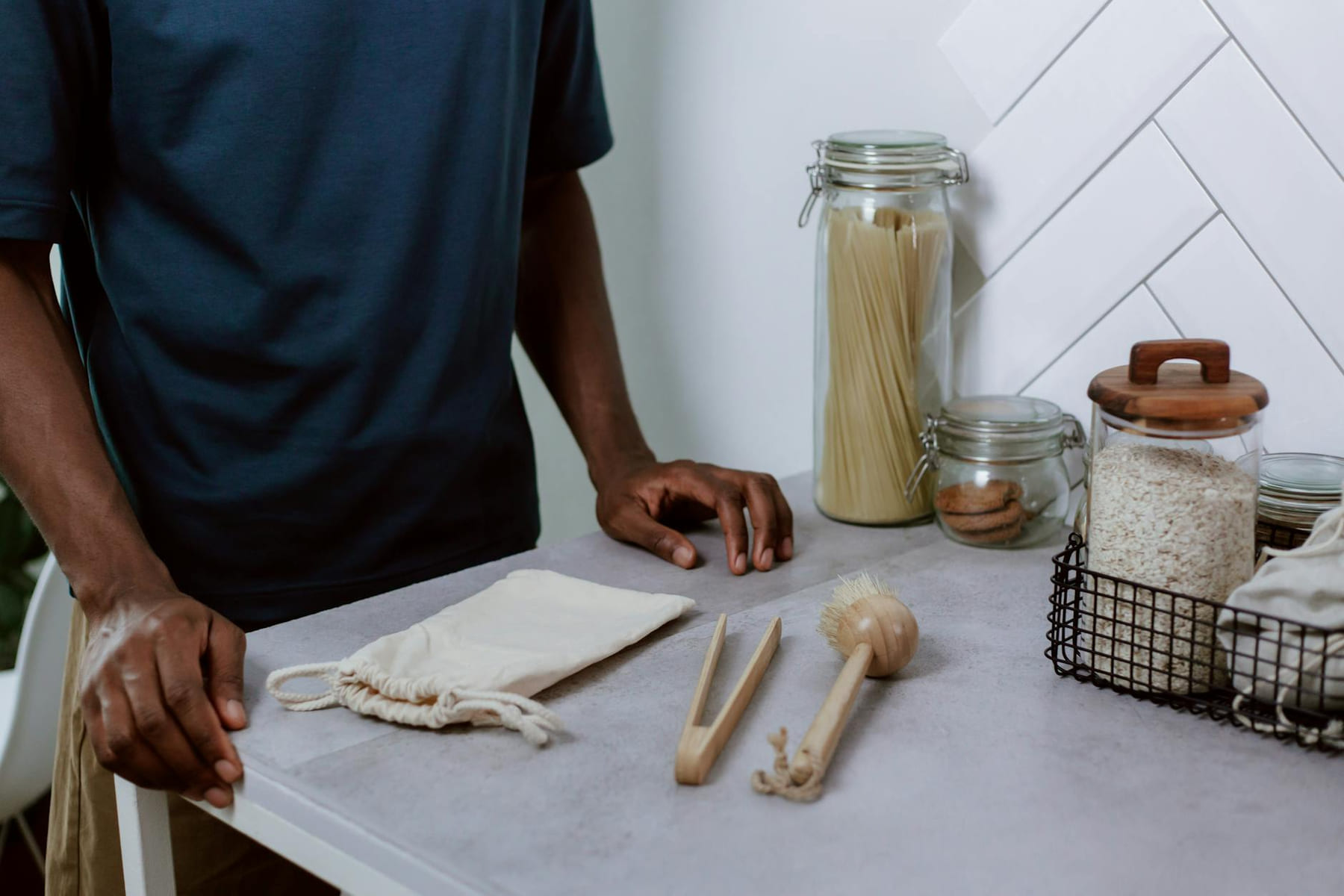 A modern kitchen counter with glass jars, utensils, and a person in a navy shirt. on Earth Wise Budget